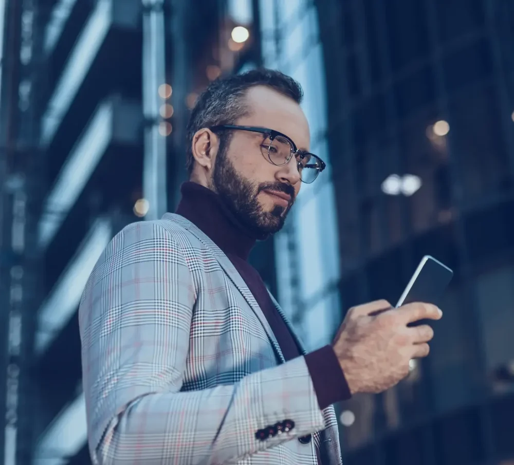 Man in glasses looking at his phone while in the city