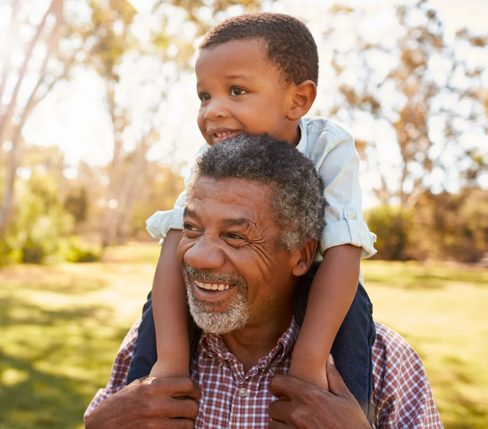 Senior man carrying grandchild on shoulders through the park