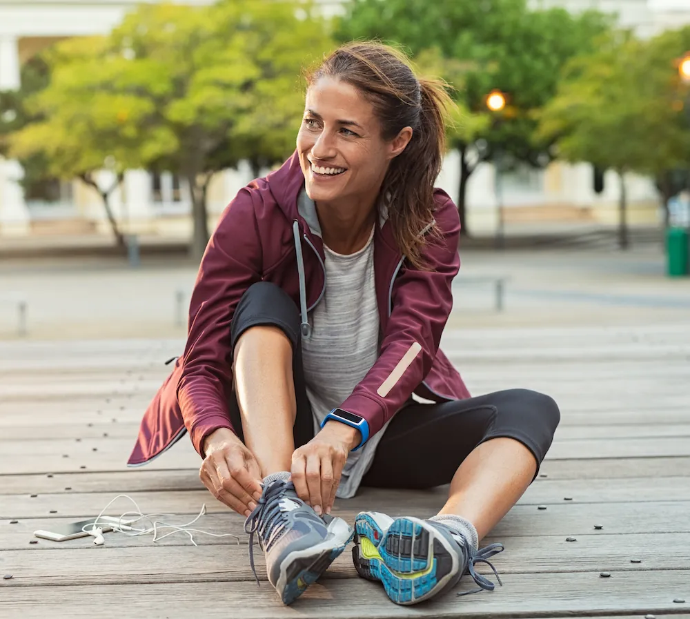Middle-aged woman in city park tying shoes before run