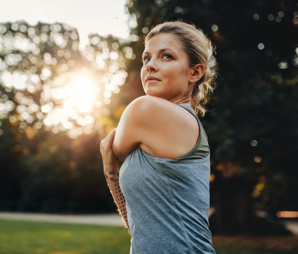Young active woman in park stretching her arm