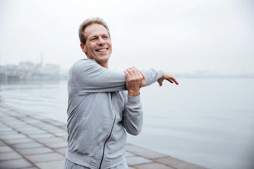 middle aged man stretching his shoulder while walking on the beach