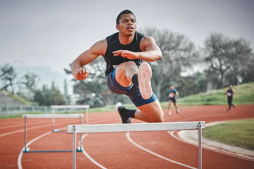 man running and jumping over a hurdle on a field track