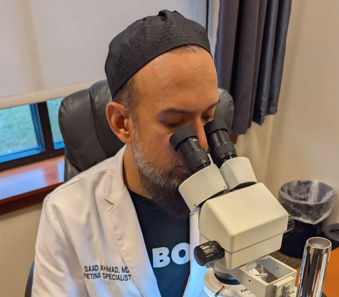 Dr. Saad Ahmad looking through a microscope looking and working on item.